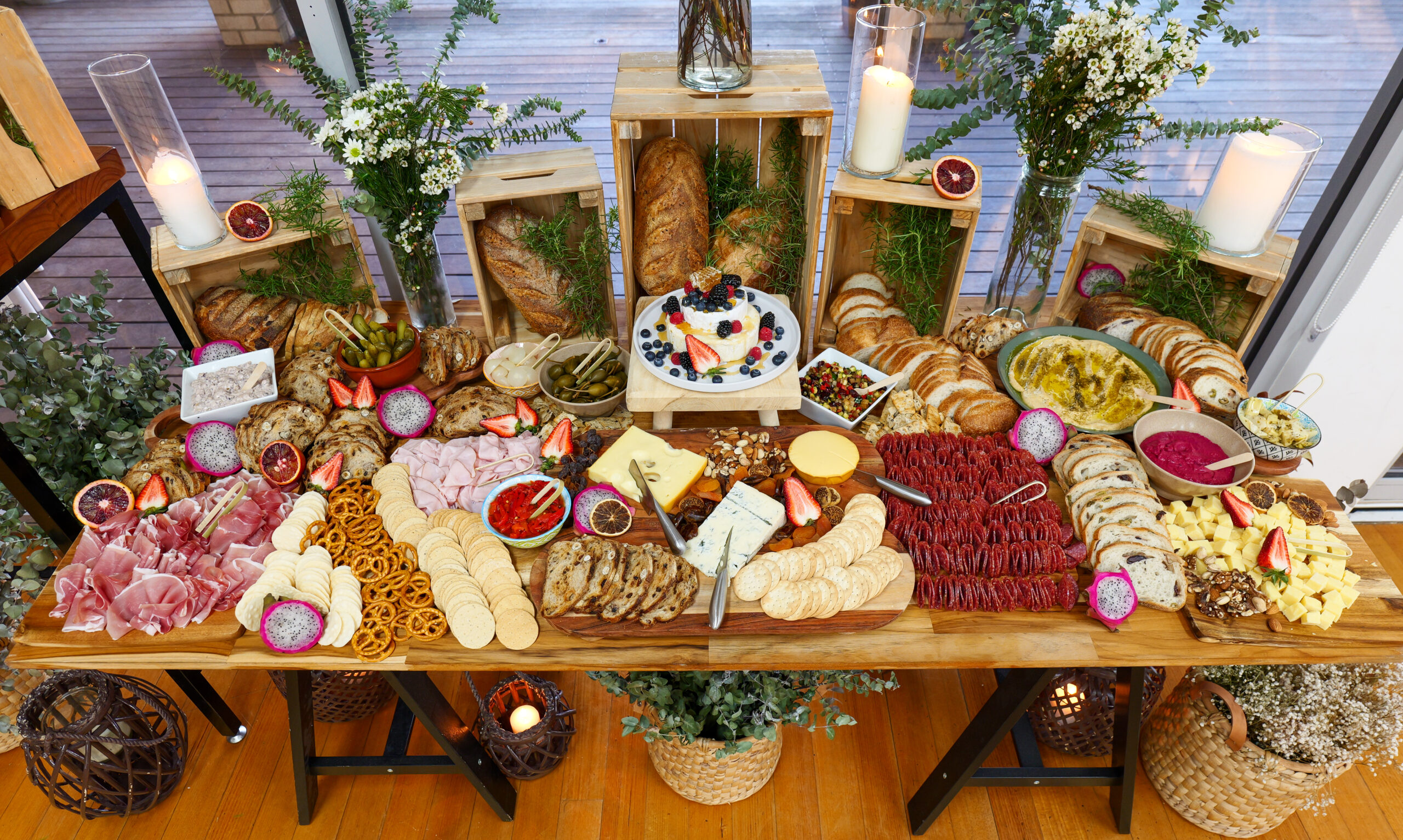 Grazing table by HLB Catering featuring cheeses, cured meats, breads, dips, fruits and antipasto beautifully arranged with candles and flowers